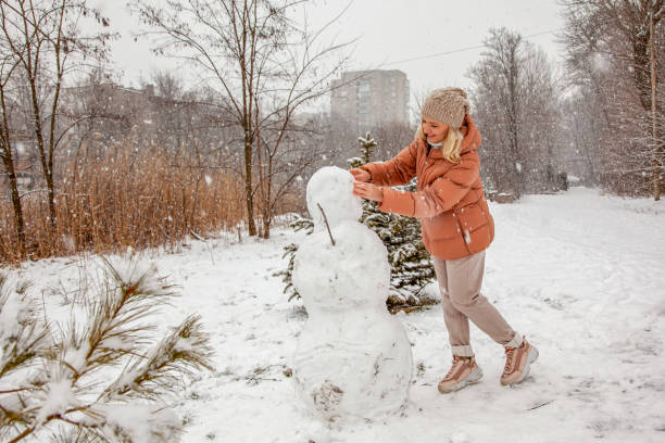 istock Woman makes a snowman in a city park during a snowfall 1425446064