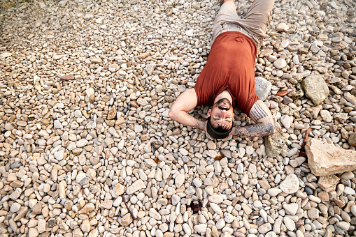 High angle view of young happy man resting on pebbles with his eyes closed. Copy space.