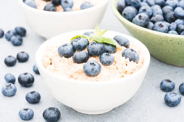 Photo of Oatmeal porridge served with blueberry and mint leaves on concrete table background. Morning superfood porridge recipe. Healthy breakfast ideas