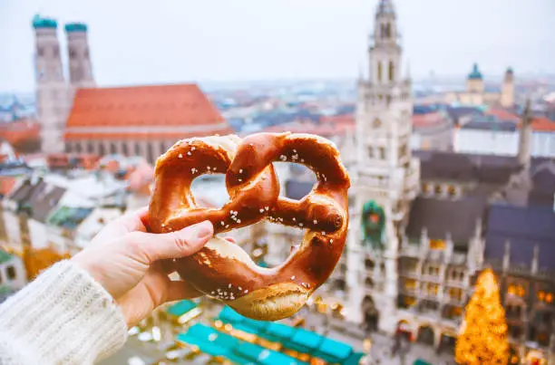 Hand with pretzel on the background of the panorama of Munich square, town hall, Christmas fair. Germany in winter. High quality photo.