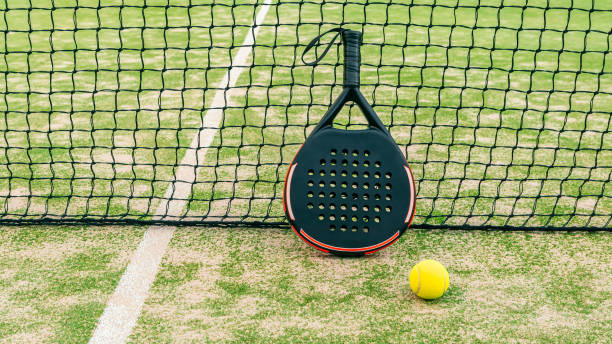 yellow ball on grass turf near padel tennis racket behind net in green court - the paddle racket imagens e fotografias de stock