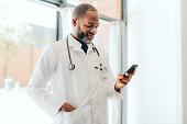 istock Medical doctor on a phone in his consultation office messaging a patient his prescription medicine. Professional black healthcare worker doing scientific research on the internet with a smartphone. 1425460352
