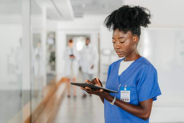 Healthcare woman, working on tablet, in medical building doctors walk, in blurred background. Young African nurse, at work in hospital or clinic, in communication or doing research via the internet. stock photo