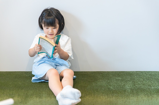 little girl reading a book alone.Kindergarten child reading a book on the sofa
