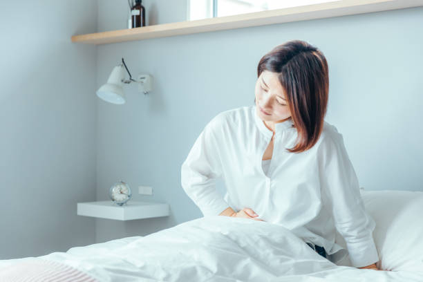 A woman holding her stomach with abdominal pain When I wake up in the morning, I am attacked by a stomachache and cannot move.Menstrual pain constipation photos stock pictures, royalty-free photos & images
