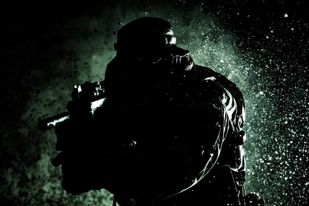 istock Commando fighter, professional mercenary, special forces soldier with camouflaged face, loaded with ammunition, armed assault rifle, patrolling on secret mission, sneaking in darkness ready to fight 1425466451