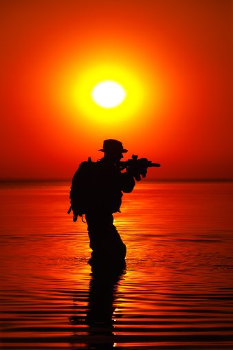 Army soldier with rifle orange sunset silhouette crossing river