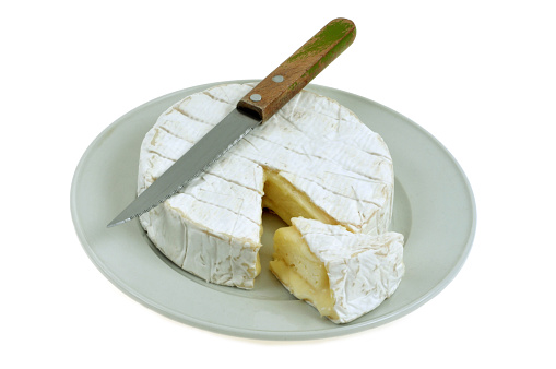 Started camembert in a plate with a knife on a white background