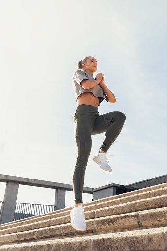 Low angle view of athletic young woman in sports clothing jumping on staircase against clear sky during sunny day