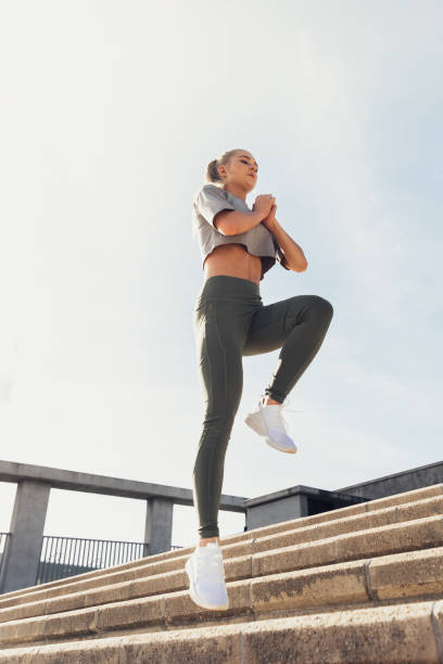 woman jumping on steps and exercising against sky - determination running staircase jogging imagens e fotografias de stock