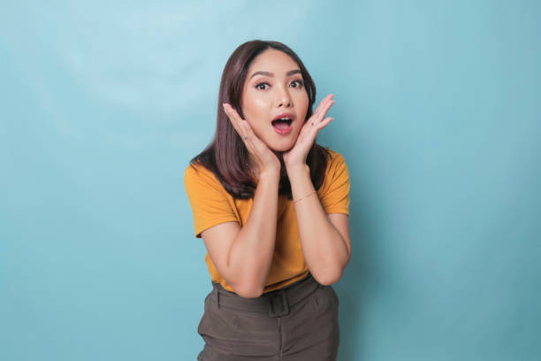 istock Surprised Asian woman reclines on her hands and shouting while looking at the camera over blue background 1425468381
