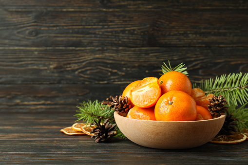 Bowl of mandarins, cones and spruce branches on rustic wooden table
