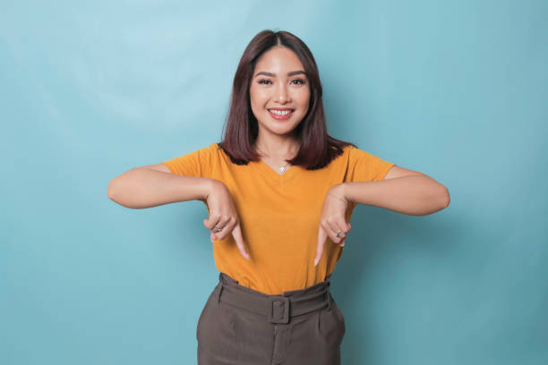 An excited young woman presenting and pointing downwards the copy space, isolated on blue background