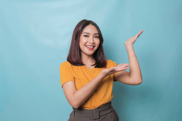 istock An excited young woman presenting and pointing copy space on her side, isolated on blue background 1425470441