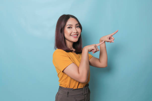 istock An excited young woman presenting and pointing copy space on her side, isolated on blue background 1425470683