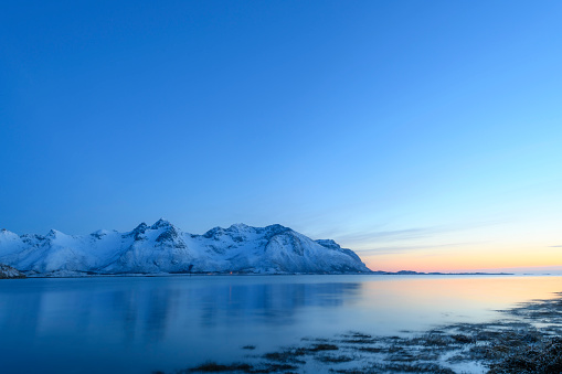 Snowy winter landscape during sunset at the shore of the Austvågøy island of the Lofoten archipel in Northern Norway The mountains are covered in snow. Long exposure image.