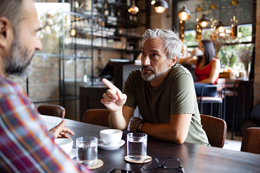 Two middle aged male friends sitting in a coffee shop, having an important conversation over a cup of coffee