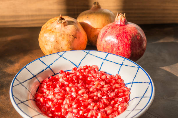 Healthy food concept. Still life with pomegranates and dish with red pomegranate grains on wooden table.
