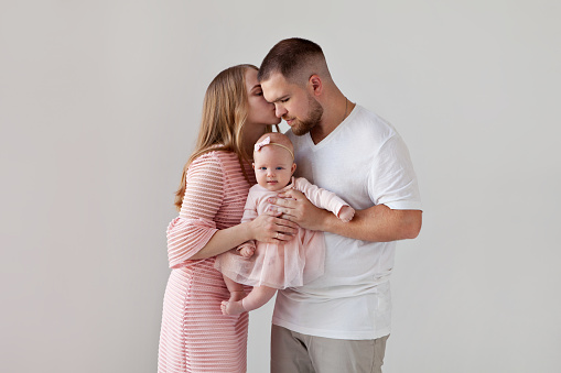 Kissing parents with beautiful little girl baby on hands. Family with daughter on isolated white background
