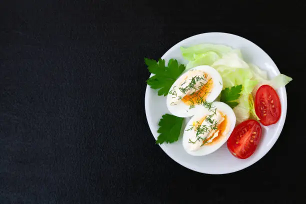 Hard boiled eggs with mayonnaise, lettuce and tomatoes on a plate - top view - copy space