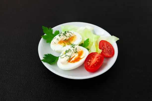 Hard boiled eggs with mayonnaise, lettuce and tomatoes on a plate - side view