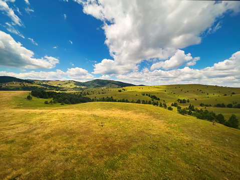 Beautiful white clouds are flowing across the sky over the green Zlatibor hills landscape on sunny summer day, popular serbian tourist travel destination from high angle view