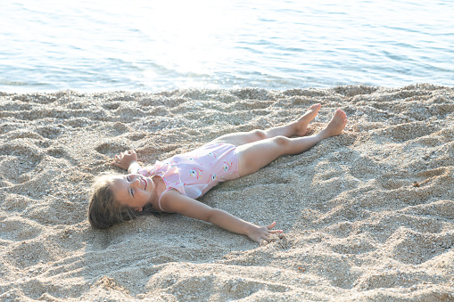 The little girl lies on the beach next to the sea. A happy child enjoys a vacation at the sea.