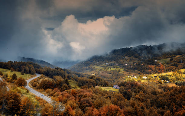 Road and village in autumn mountain forest, beautiful bright landscape with cloudy dramatic sky stock photo
