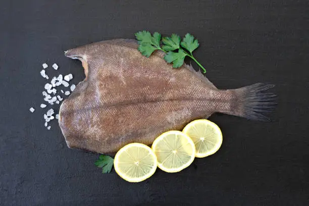 Fresh flounder with lemon and herbs close-up - preparation for cooking a fish dish - top view