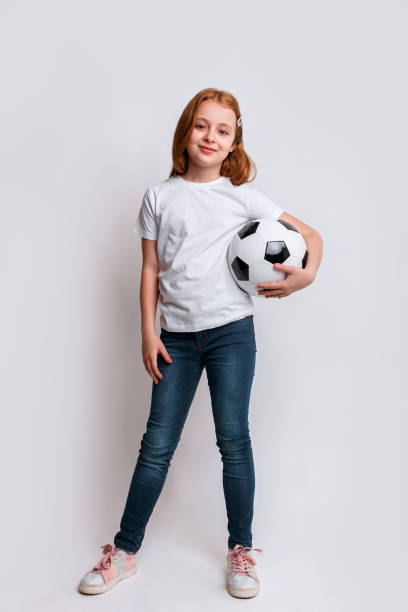 Cute little kid dreams of becoming a football player. Redhead girl with football. stock photo