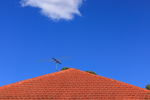 Antenna on a red tiled roof against a blue sky.