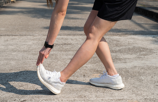 Foto recortada de una corredora haciendo estiramientos y calentando sus piernas antes de correr en el parque público. photo