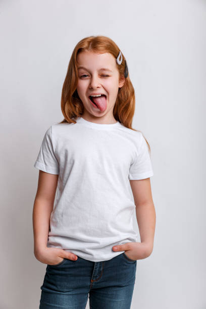 Portrait of funny kid girl smiling and showing tongue in camera wearing in white t-shirt. Close-up kid portrait stock photo
