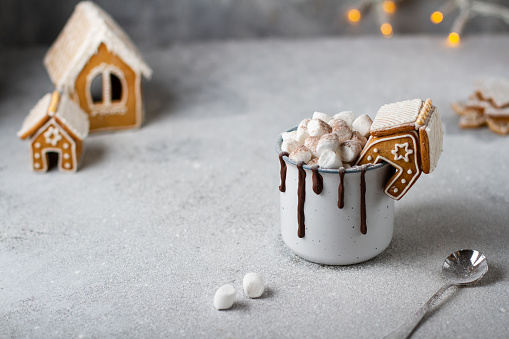 Gingerbread house on a mug with cocoa and marshmallows, chocolate drips, light gray background, gingerbread, garland, free space