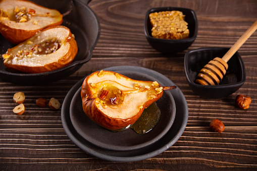 Honey or maple syrup roast pears with walnuts on wooden background. Vegetarian diet health delicious dessert. Top view.
