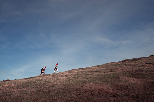 Fanal, Madeira, Portugal - September 16, 2022: Two people walking up hill on a steep slope with the blue dramatic sky in the background. Minimalist photography in moody tones with negative space