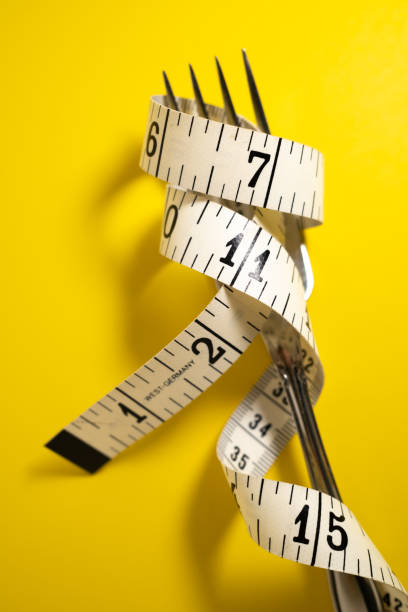 istock Silver Fork with Measuring Tape Wrapped Aroung It on a Yellow Background 1425519114