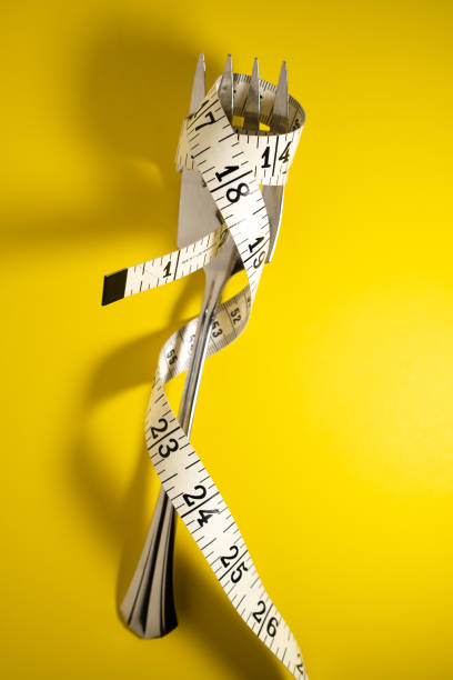 istock Silver Fork with Measuring Tape Wrapped Aroung It on a Yellow Background 1425519117