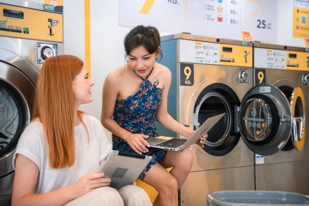 istock Two women are using laptops and talking in the laundry area. while waiting for the washing machine to work 1425519222