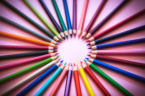 Back to school concept with colored pencils arranged in a circle on pink background. Close up. Art and craft. Design professional.  Education. Office supplies. Flat lay. Copy space. Top view.