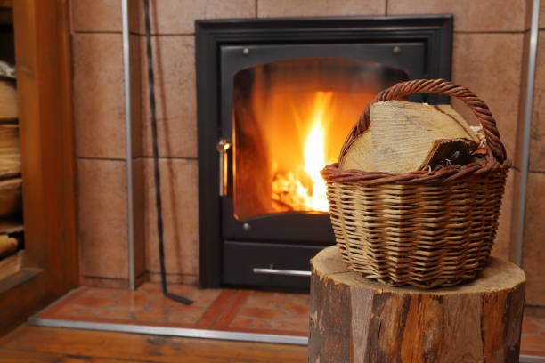 A wicker basket of birch logs on a timber stump against the background of a fireplace with burning firewood.