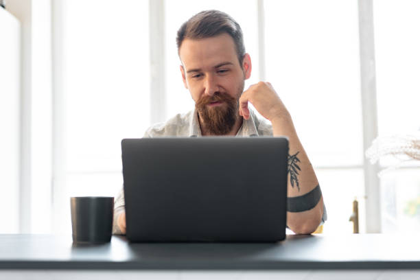 istock Stylish bearded man working on laptop from home sitting at the table 1425530500