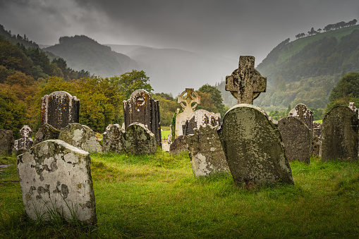 Ancient graves with Celtic crosses in Glendalough Cemetery. Autumn forest in mountains, Wicklow, Ireland