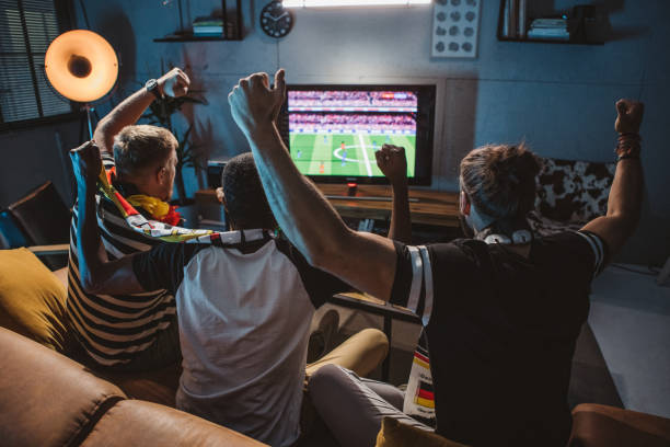 Watching soccer championship at home Diverse group of men watching soccer match at home and cheering for Germany team. tv game stock pictures, royalty-free photos & images