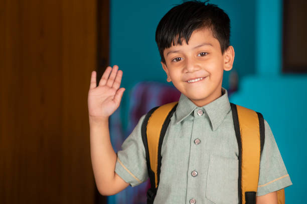 Portrait of a little school boy in uniform with backpack waving hand. Portrait of a happy Indian little boy in school uniform with backpack waving a hand to the camera with a smile. . kid waves stock pictures, royalty-free photos & images