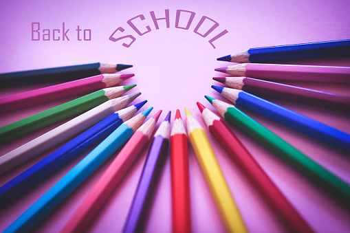Back to school concept with colored pencils arranged in a circle on pink background. Colored font. Close up. Art and craft. Design professional.  Education. Office supplies. Flat lay. Copy space. Top view.