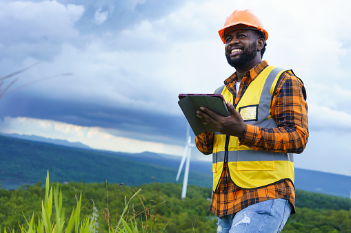 Black Engineer wearing safety jacket and hardhat holding tablet while working at outdoor, Smart working lifestyle.
