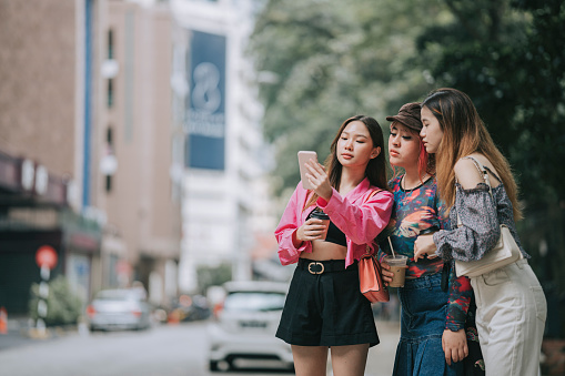 Asian young woman and friends hailing a ride taxi using her mobile app