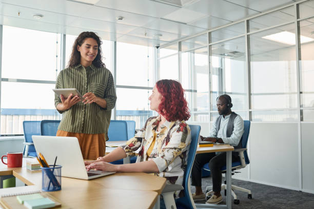 istock Happy young office worker with tablet communicating with female colleague 1425544018