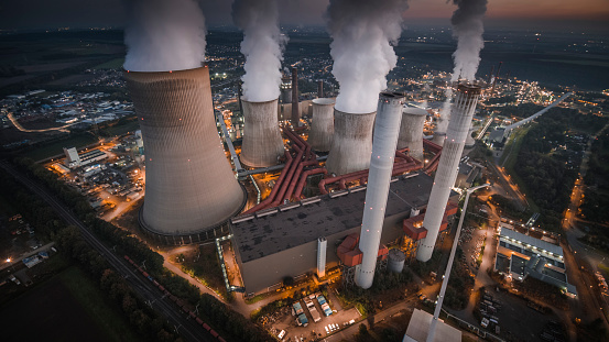 Aerial view of building exterior from a coal fired power station at night. Large cooling towers emitting steam into to air. Great for global warming, climate change and pollution themes. With its lights already turned on the power station is illuminated in moody twilight.
